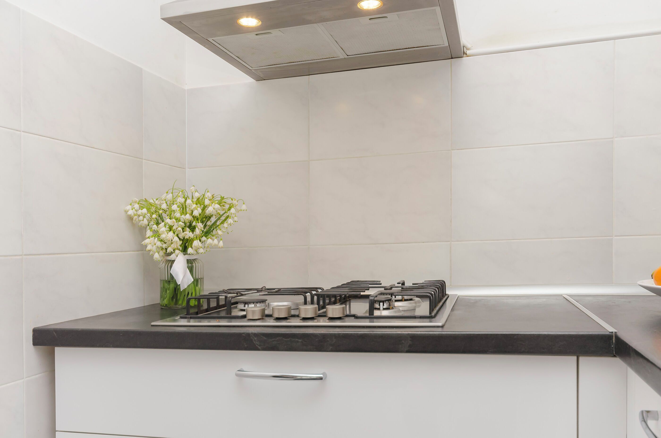 A kitchen with white tiles, a gas stove, and a vase with flowers on the counter.
