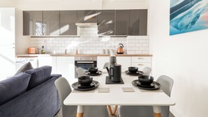 A modern kitchen with white cabinets, a dining table set with black plates and bowls, and a gray sofa in the foreground. - Stunning 5-bed Maisonette in Bristol (Bristol)