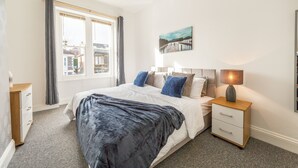 A bedroom with a large bed, a bedside table with a lamp, a dresser, and a window with curtains. - Stunning 5-bed Maisonette in Bristol (Bristol)