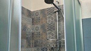 A shower with a glass door, a handheld showerhead, and a wall with patterned tiles.