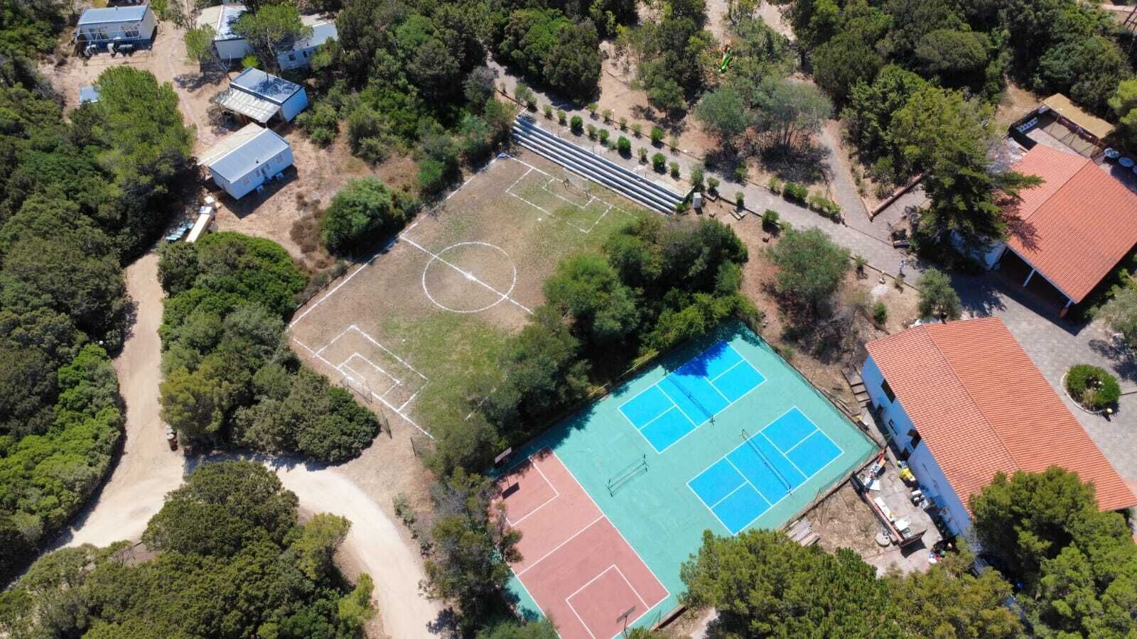 Vista aérea de una propiedad con cancha de tenis, cancha de baloncesto y varios edificios rodeados de árboles.