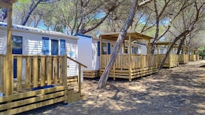 A row of mobile homes with wooden decks and a tree in the foreground. - HappyCamp in Camping Baia Paradiso (Badesi)