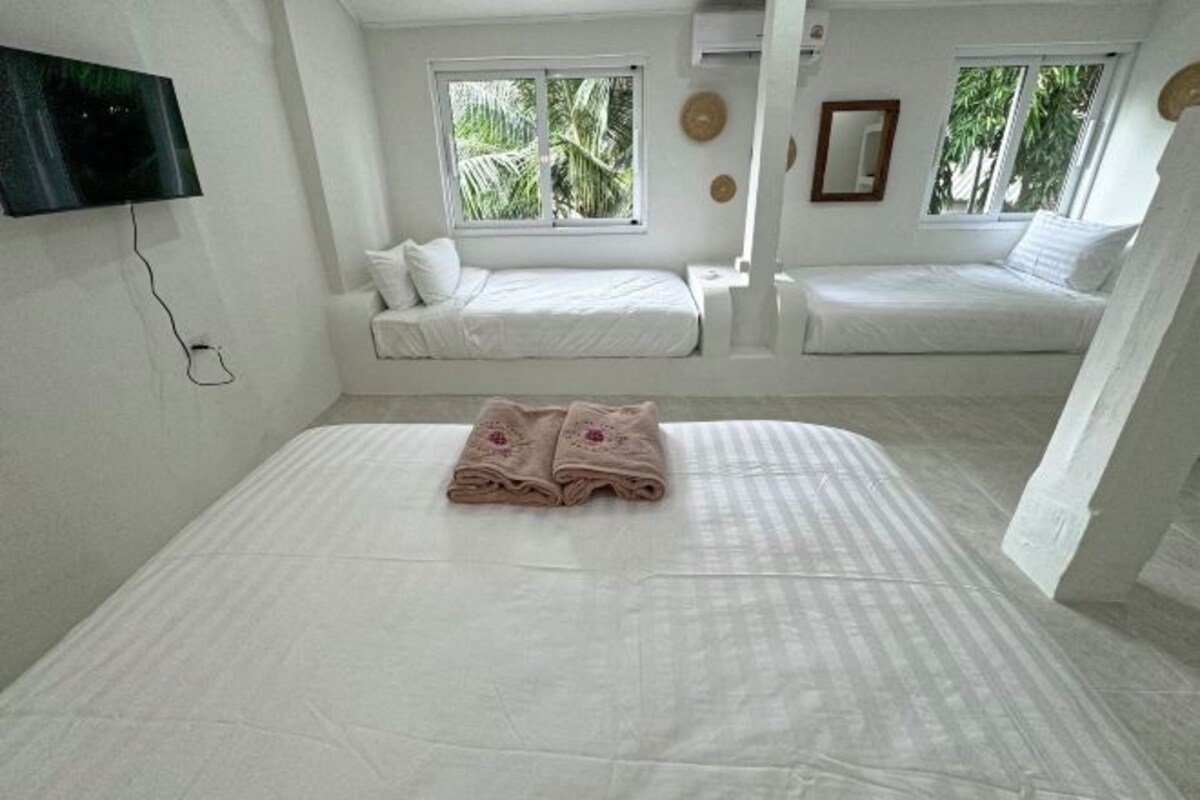 A room with two beds, a flat-screen TV mounted on the wall, and windows with a view of greenery.