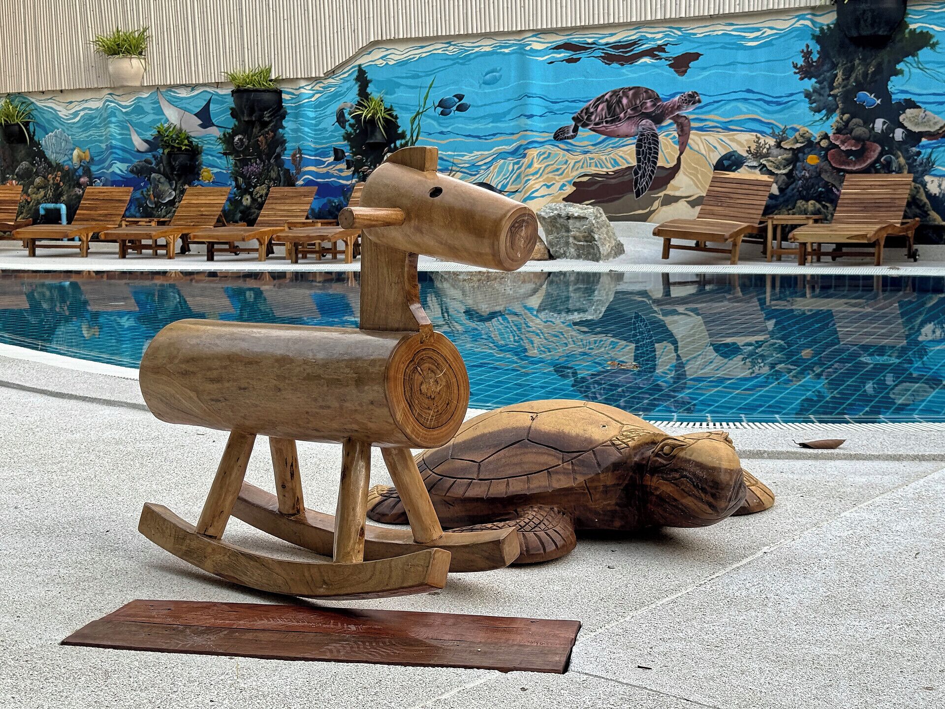 Une sculpture en bois représentant une tortue, placée près d’une piscine, avec une fresque représentant la vie marine en arrière-plan.