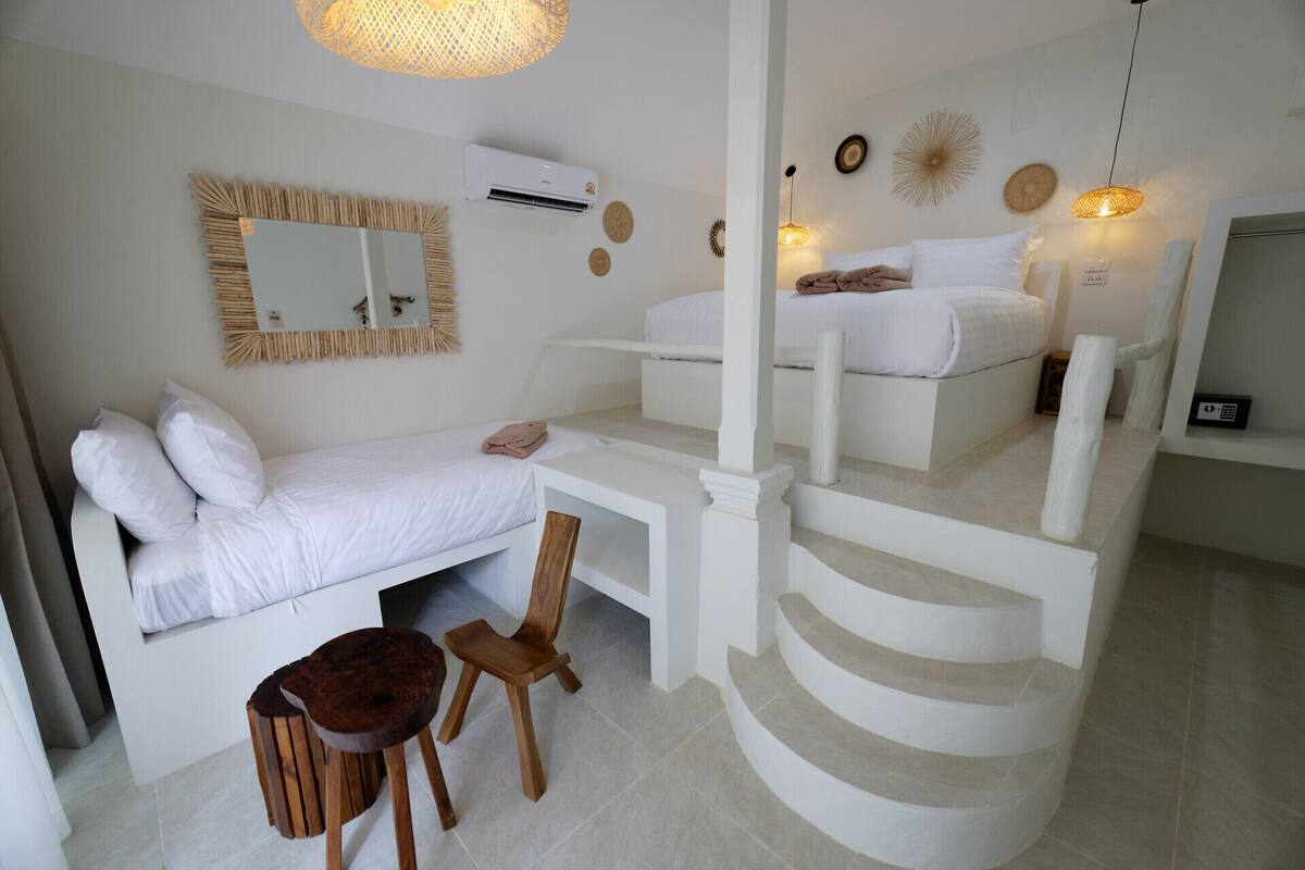 A bedroom with a bed, a desk, a chair, a staircase, and a mirror.
