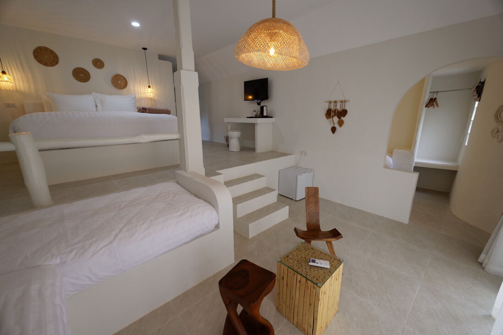 A modern bedroom with a large bed, a small wooden stool, and a TV on a white console table.