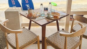 A table with two chairs, a surfboard, and a view of the beach with boats. - Blue Turtle Hotel Samui (Koh Samui)
