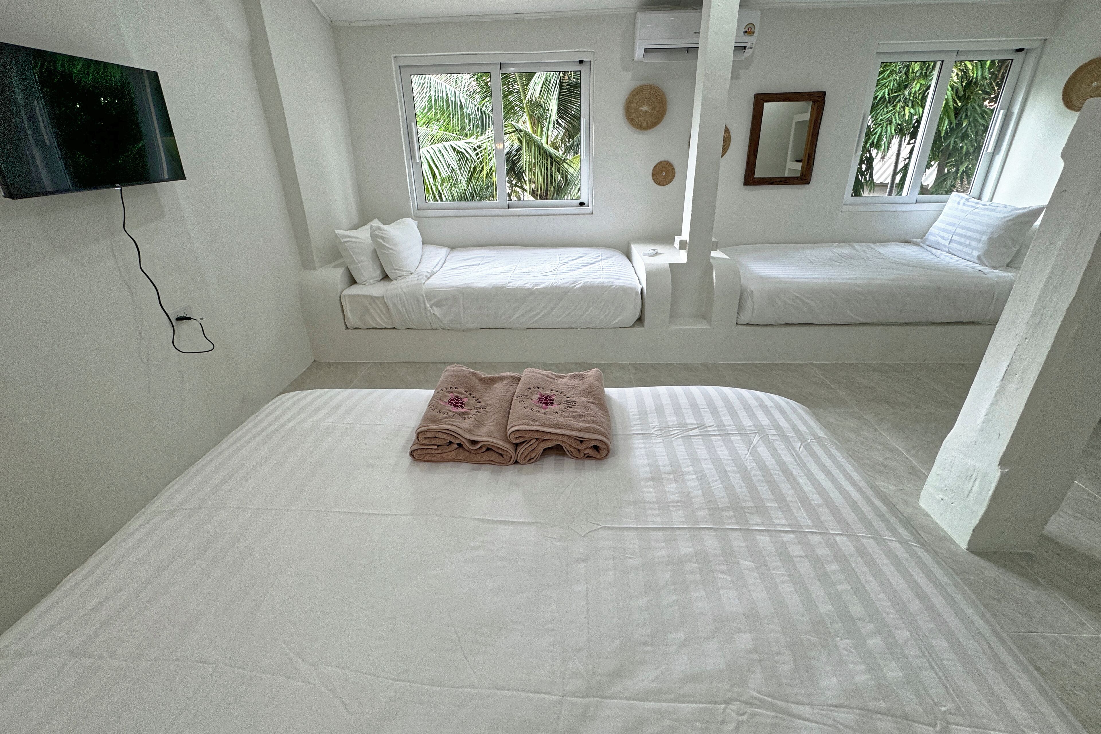 A room with two beds, a flat-screen TV, and a window with a view of palm trees.