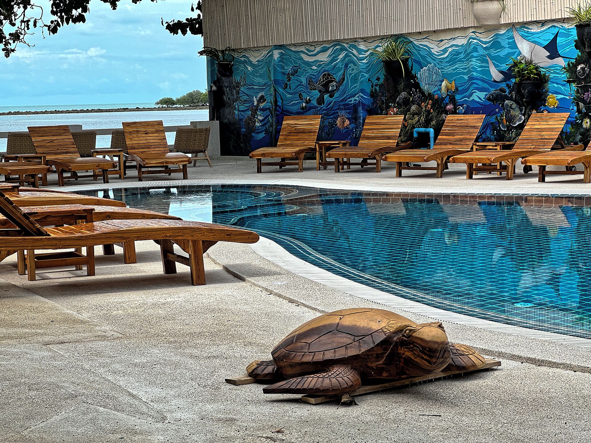 A pool area with wooden loungers and a mural of sea life.