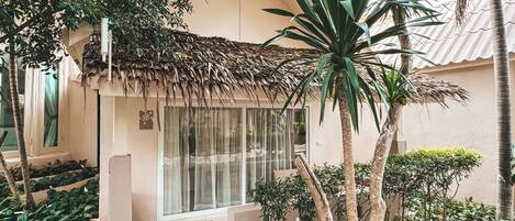 A building with a thatched roof, surrounded by lush greenery and palm trees.