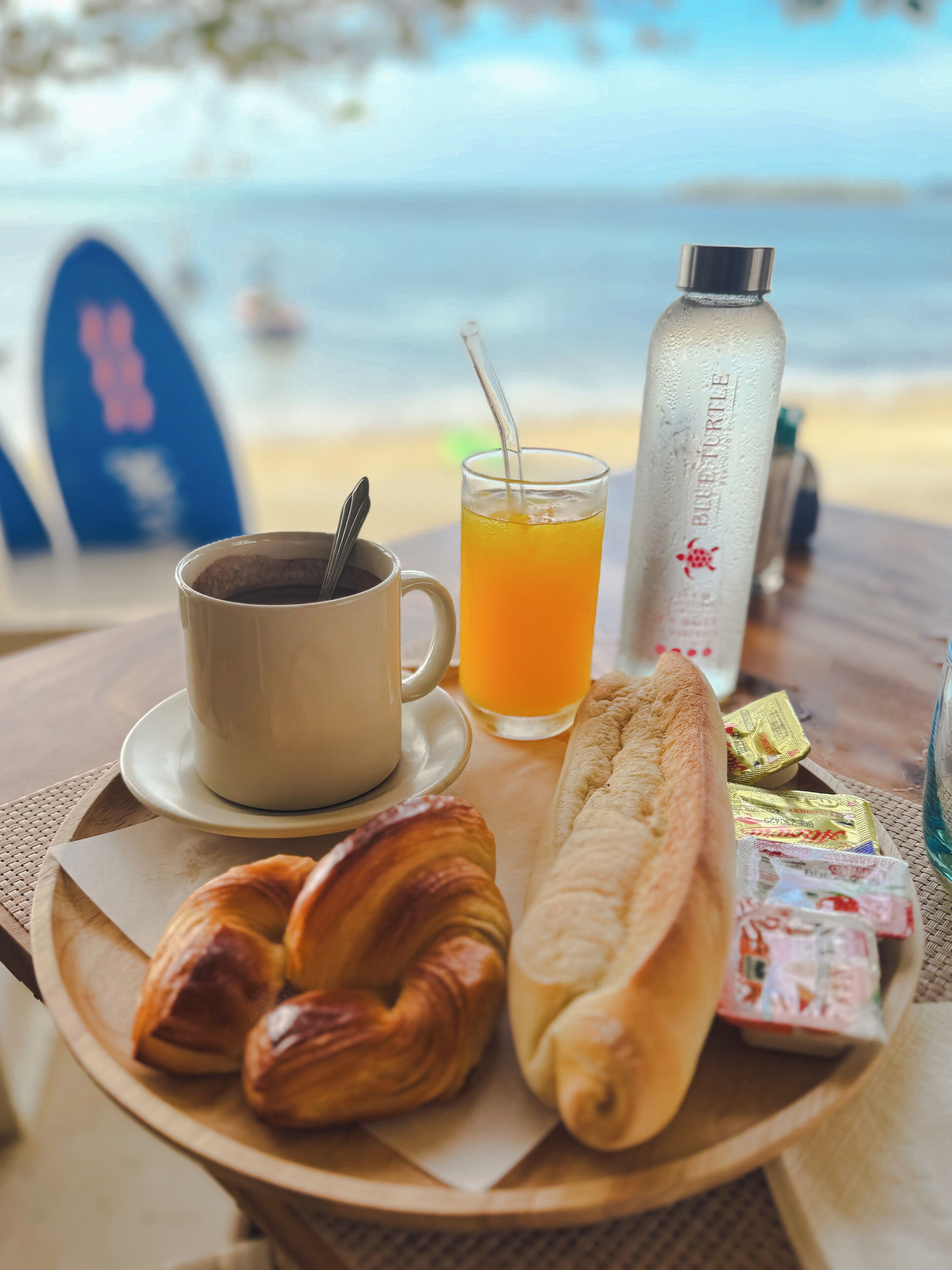 Un plateau de petit-déjeuner avec des croissants, une tasse de café, un verre de jus d’orange, une bouteille d’eau et quelques en-cas emballés.