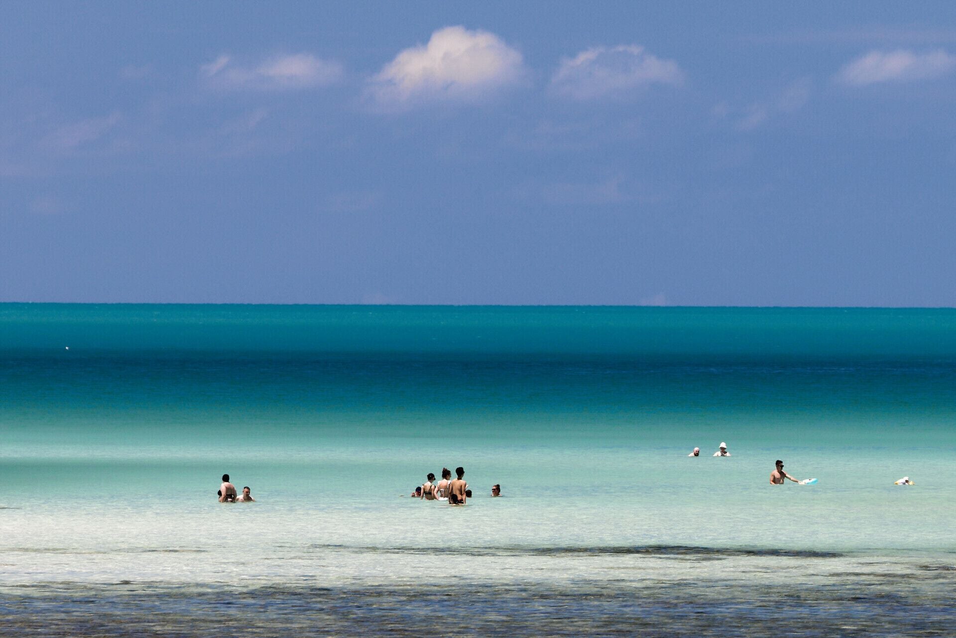 A beach with clear turquoise water and a few people swimming and sunbathing.
