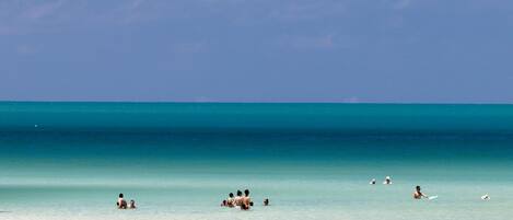 A beach with clear turquoise water and a few people swimming and sunbathing.
