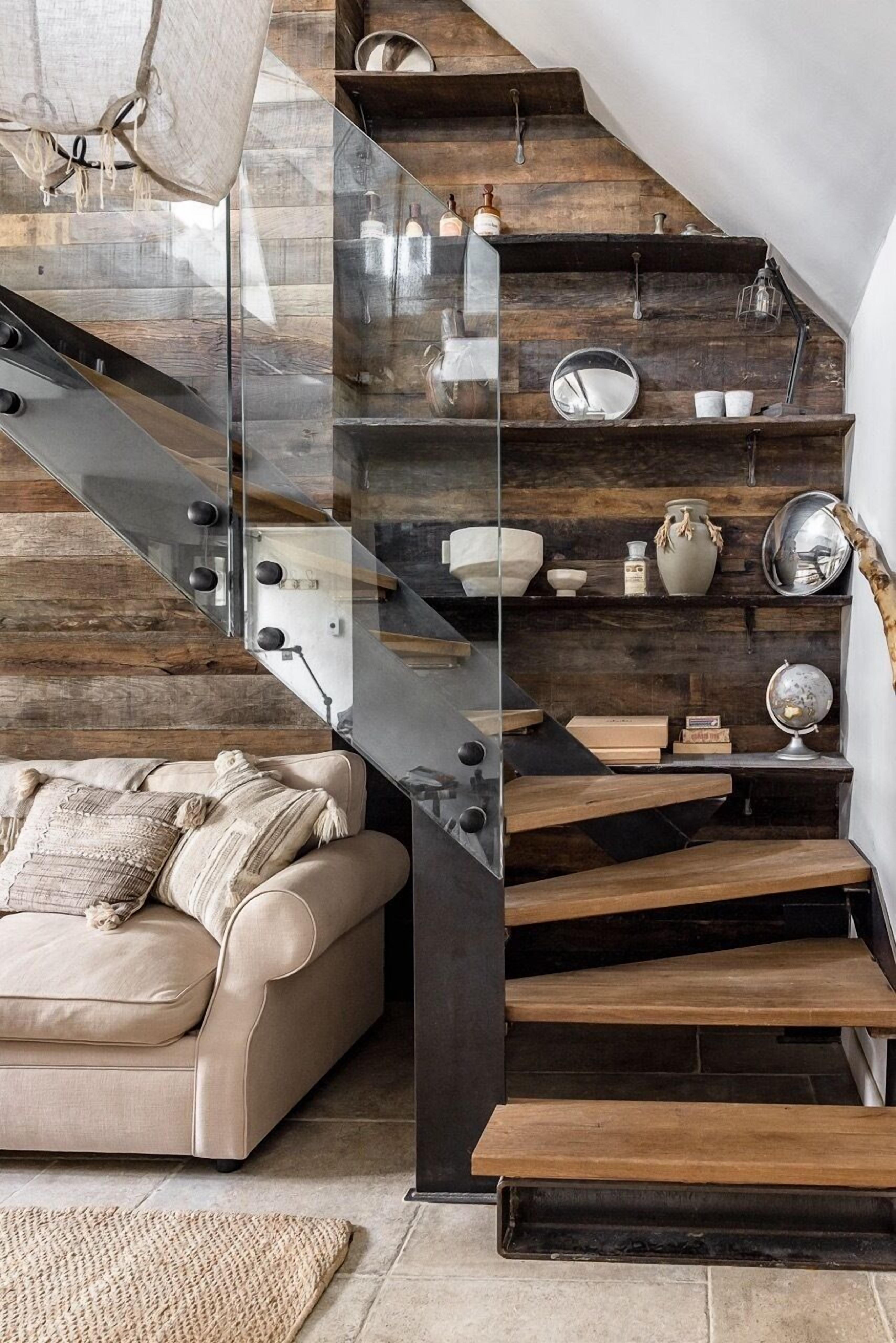 A modern staircase with glass railings and wooden steps, leading to a living area with a sofa and decorative items.