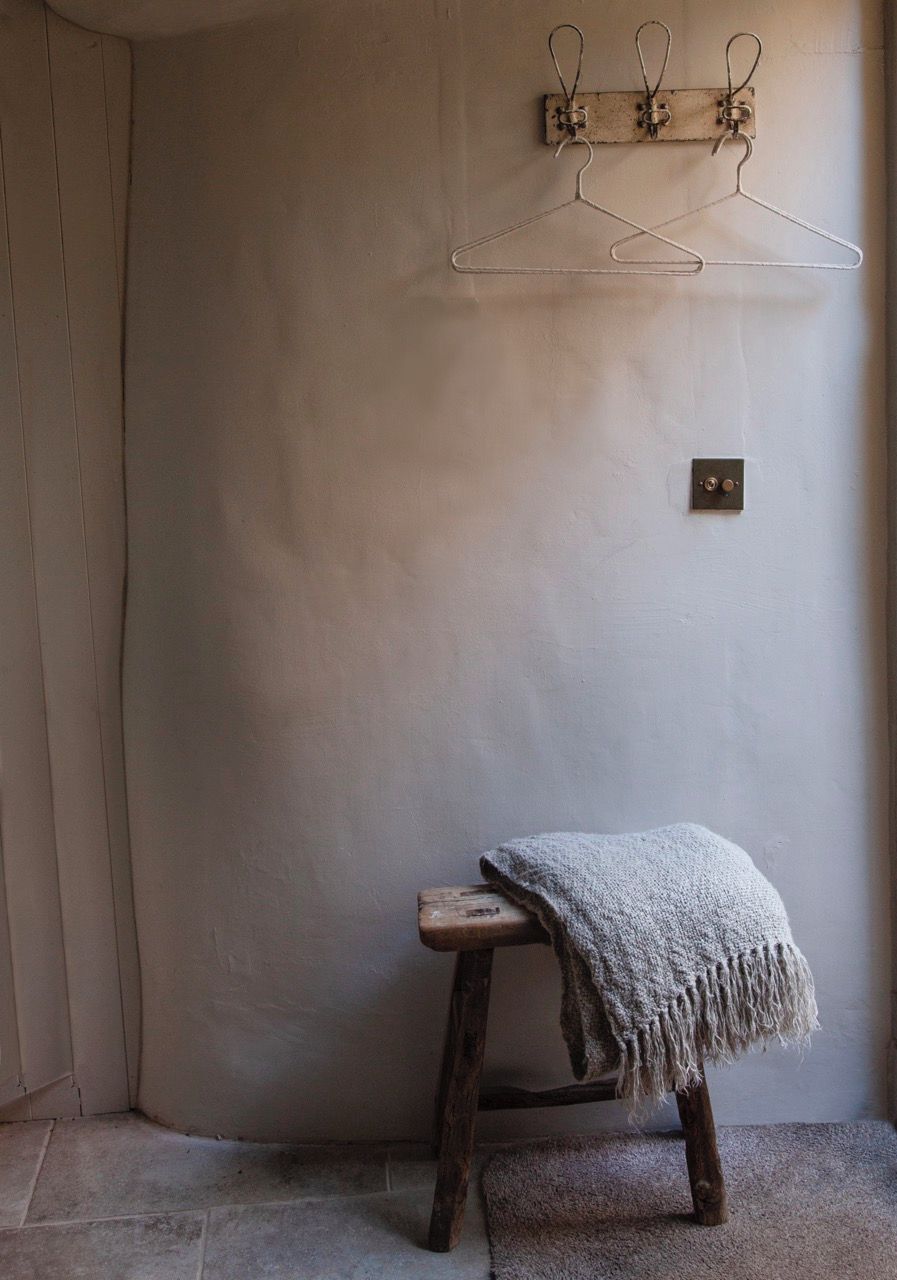 Un coin de pièce avec un tabouret en bois, un porte-vêtements suspendu et un interrupteur sur le mur.