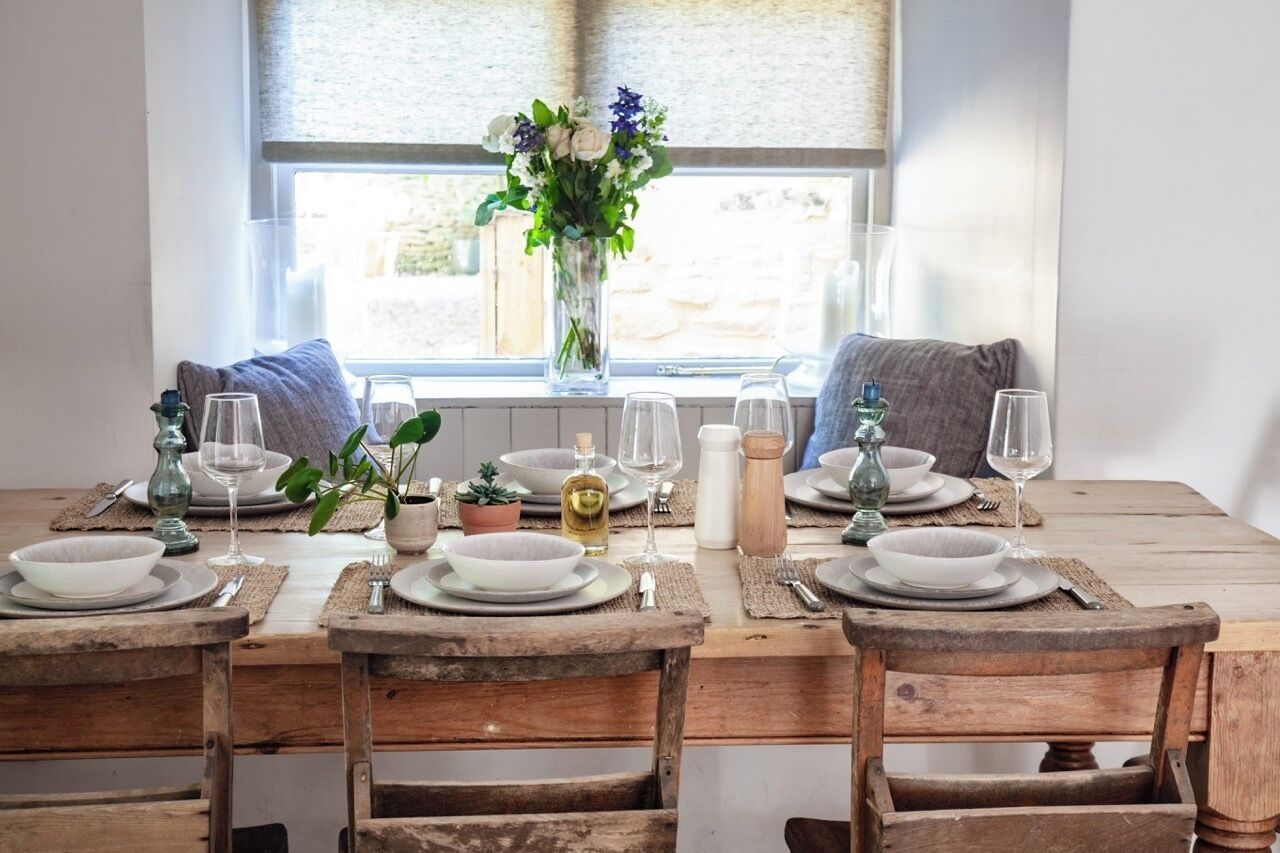 Un tavolo da pranzo in legno apparecchiato con piatti, bicchieri e un vaso di fiori.