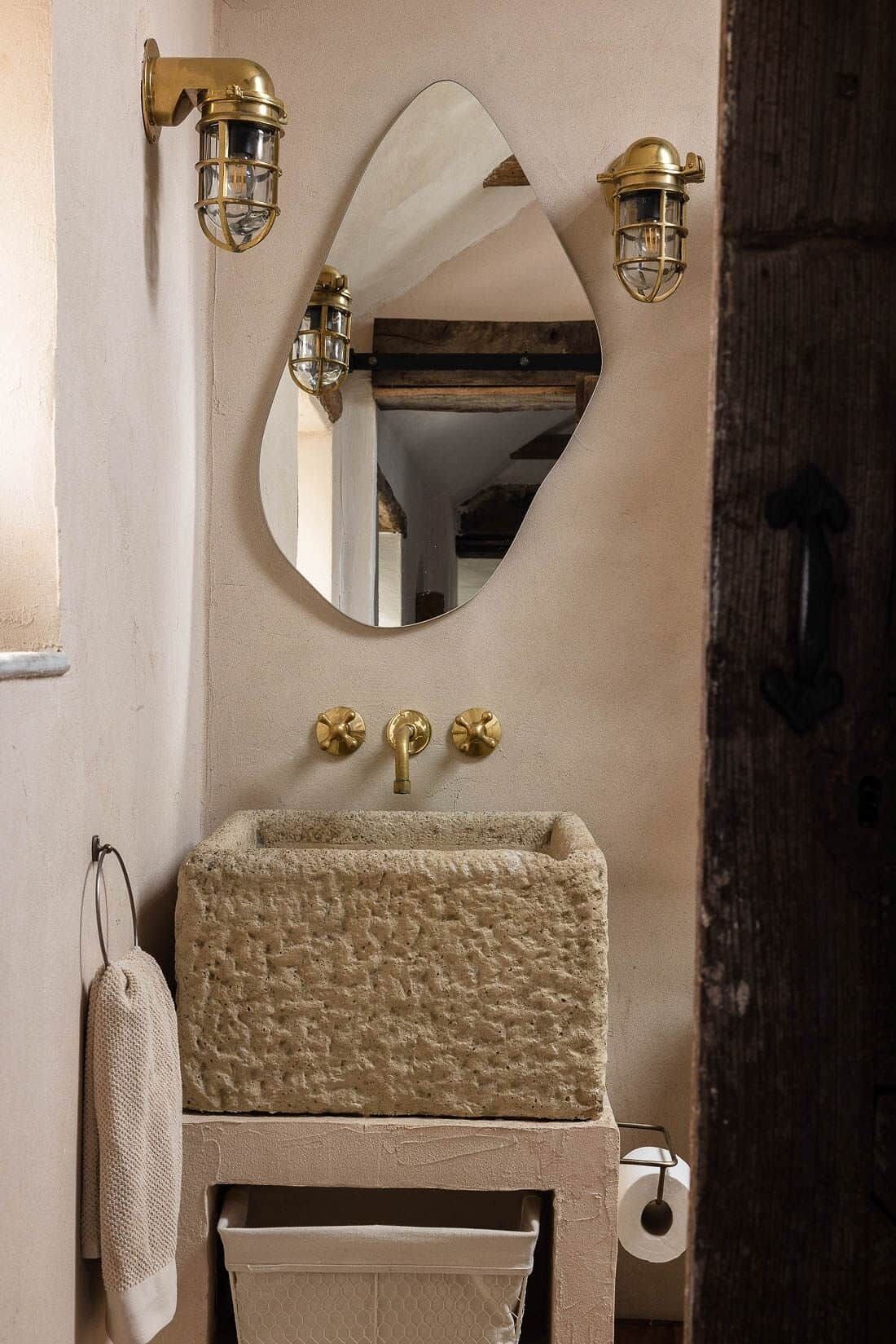A bathroom with a stone sink, a mirror, and brass fixtures.
