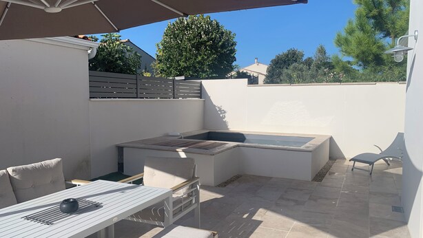 Eine Terrasse im Freien mit Tisch, Stühlen, einer Bank, einem Grill und einem großen Sonnenschirm.