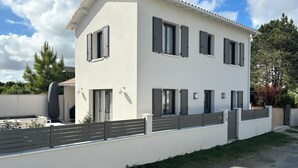 Ein zweistöckiges Haus mit weißer Fassade, zahlreichen Fenstern mit Fensterläden und einem grauen Zaun.