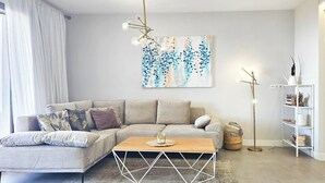 Una sala de estar moderna con un sofá seccional, una mesa de centro de madera, un tapete blanco geométrico, una lámpara de pie y una estantería.