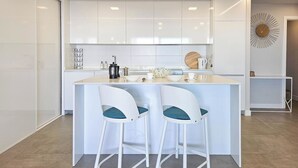 Una cocina moderna con armarios blancos, una isla central con dos taburetes de bar y un elemento decorativo en la pared.