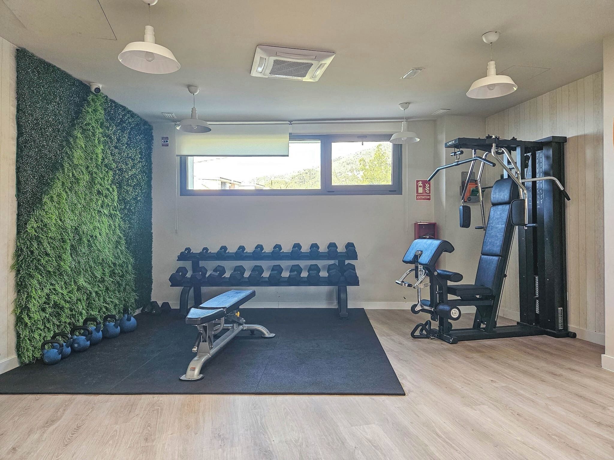Ett gym med träningsredskap, en bänk och en vägg som är täckt av grönska.