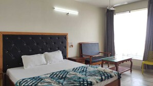 A hotel room with a bed, a chair, a table, and a window with curtains. - Tarangamala Resort (Kanthi)