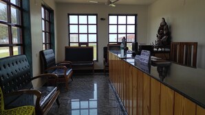 A reception area with a counter, seating, and large windows. - Tarangamala Resort (Kanthi)