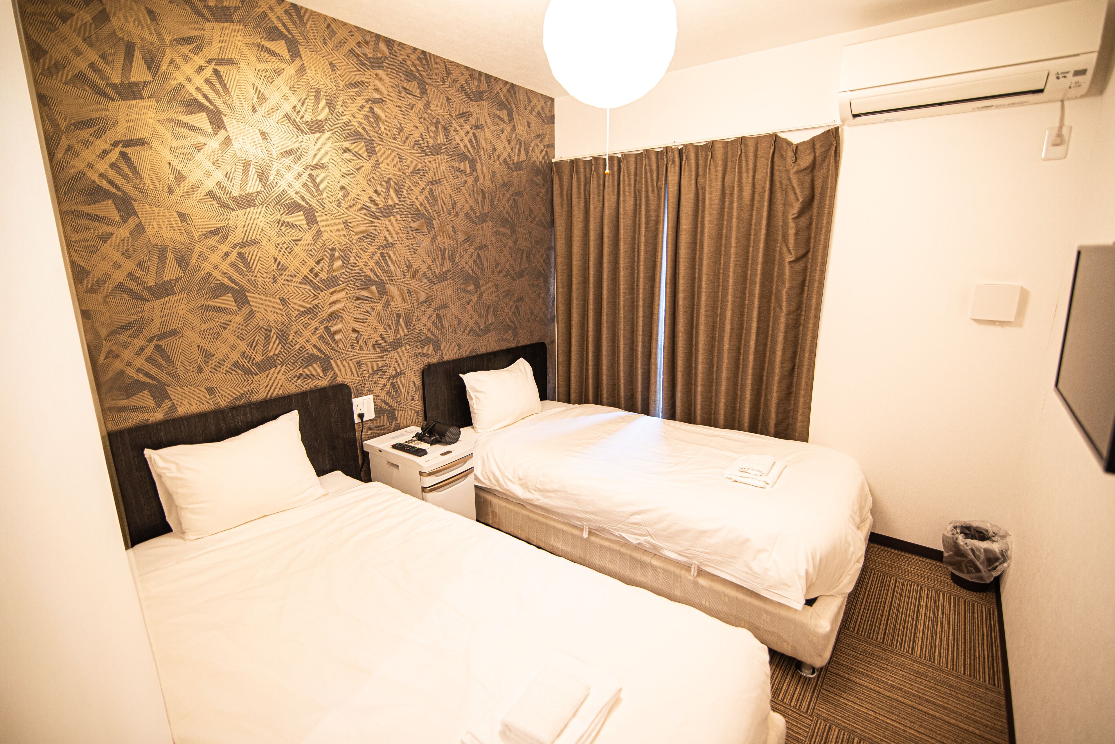 Habitació d'hotel amb dos llits, una tauleta de nit, un telèfon i aire condicionat fixat a la paret.