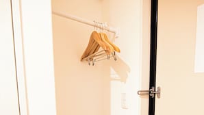 Ein Hotelzimmer mit Tür, Kleiderhaken mit Kleiderbügeln, einem Besen und einem Lichtschalter an der Wand.