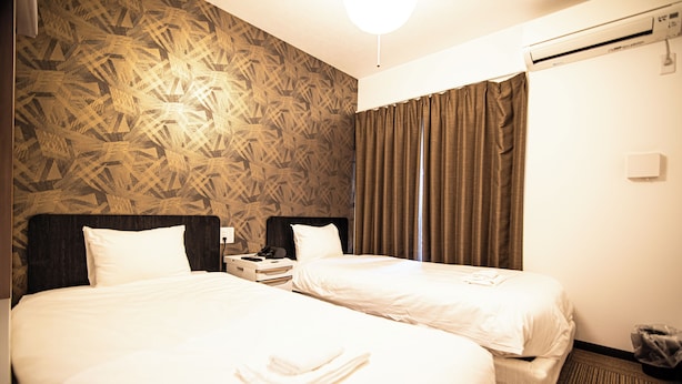 Ein Hotelzimmer mit zwei Betten, einer gemusterten Wand, einem Nachttisch und einer Klimaanlage.