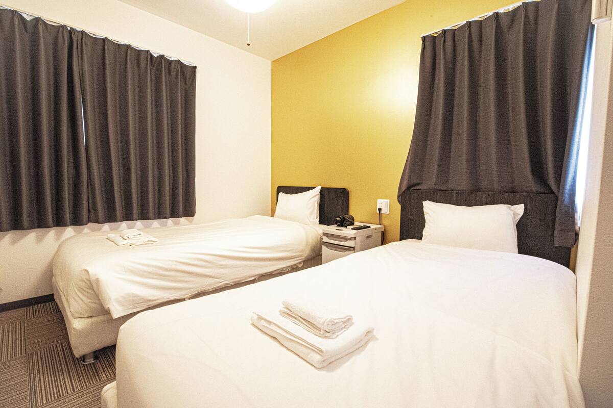 Una habitació d'hotel amb dos llits, una tauleta de nit i un telèfon fixat a la paret.