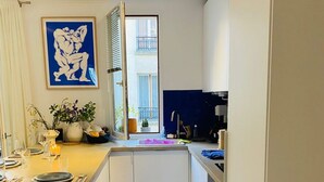A compact kitchen with a dining area, a window with a view, and a blue floor. - Chic 3 Pièces Familial Pour Bébé au Cœur de Paris (Paris)