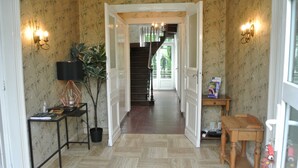 Ein Korridor mit ornamentalem Wandpapier, einer Treppe, einem Holztisch und einer Zimmerpflanze.