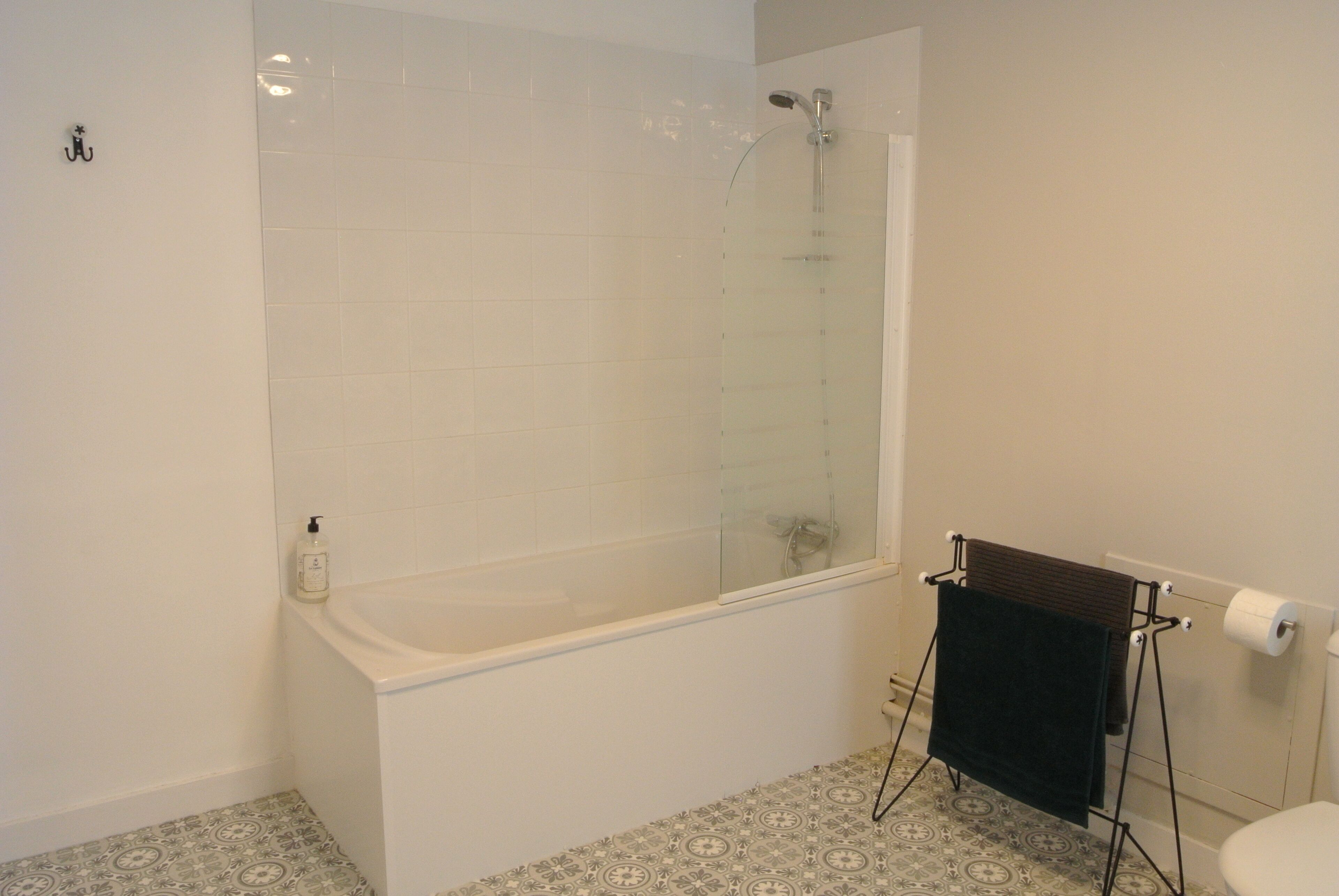 A bathroom with a glass-enclosed shower, a white bathtub, patterned floor tiles, and a towel rack.