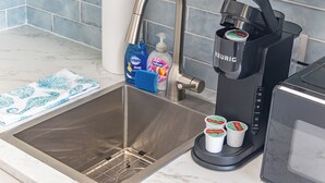 Een keuken met een roestvrijstalen spoelbak, een zwarte koffiezetapparaat en twee theecornetten.