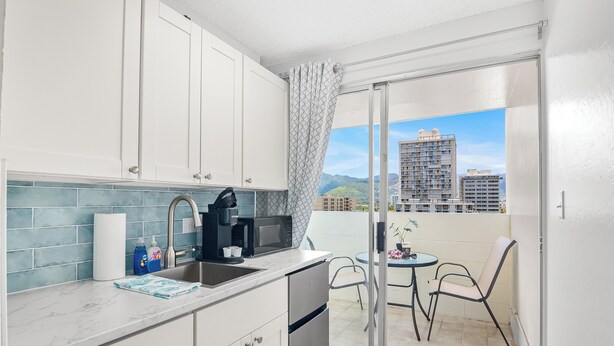 Een moderne keuken met witte kastjes, een marmeren aanrechtblad en uitzicht op een balkon met een tafel en stoelen.
