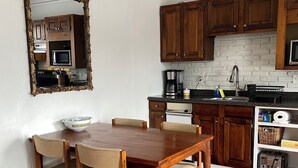 A dining area with a wooden table and chairs, a kitchen with wooden cabinets and a brick backsplash, and a white ceiling with decorative molding.
