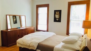 A bedroom with a bed, wooden dresser, two windows, and a wall-mounted mirror.