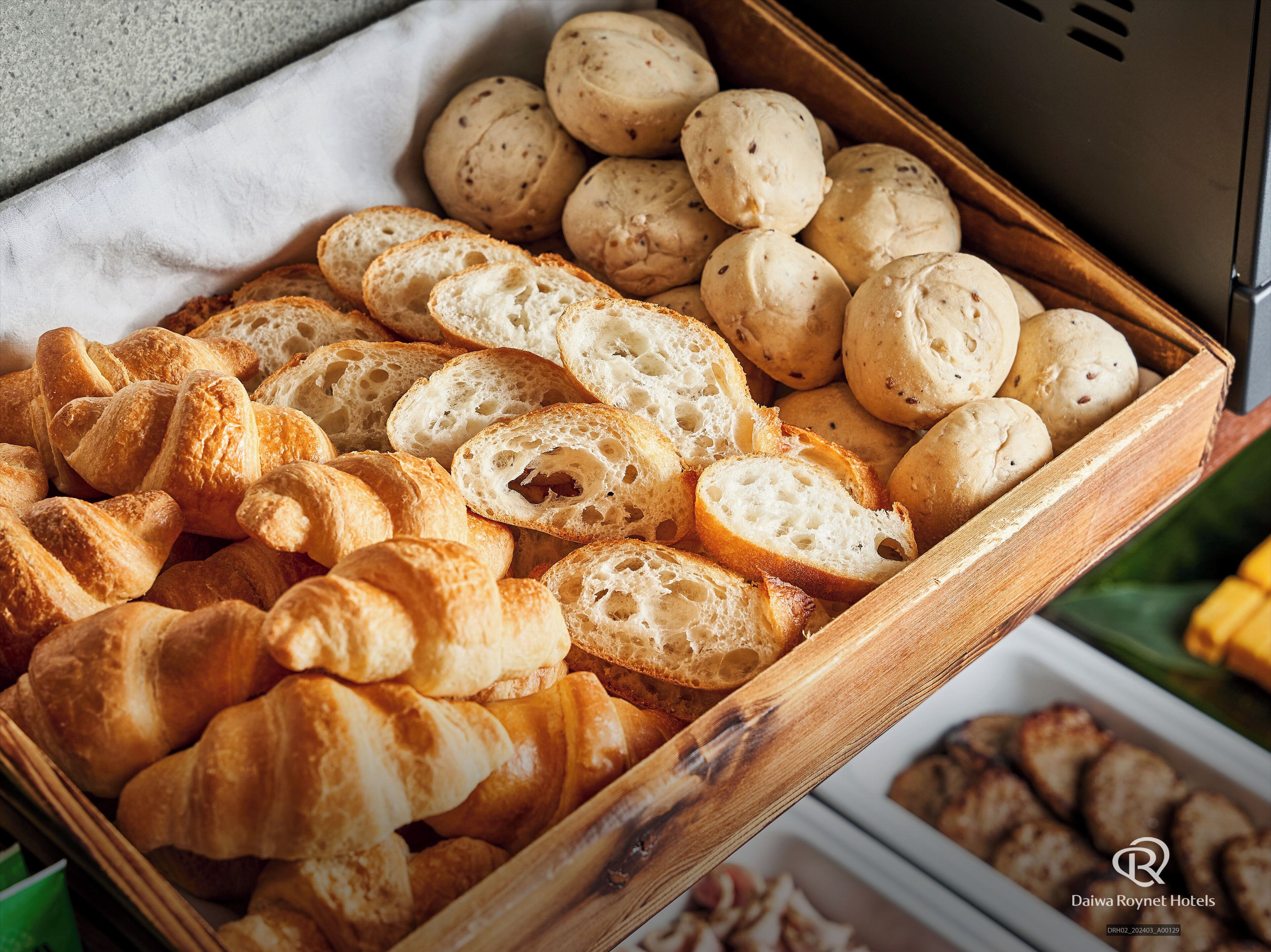 A wooden tray filled with various types of bread, including croissants and round bread rolls.