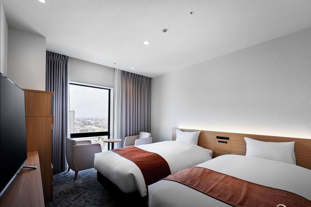 Habitación de hotel con dos camas, televisión, escritorio y vistas a la ciudad.