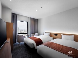 A hotel room with two beds, a TV, a desk, and a view of the city.
