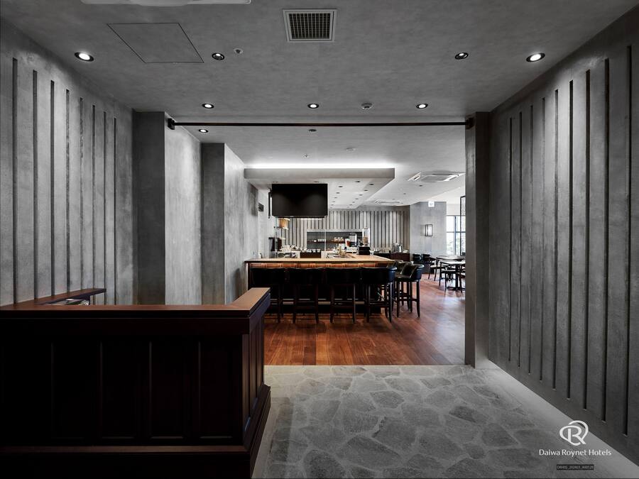 A modern hotel lobby with a central bar area, stone flooring, and a view of the dining area.