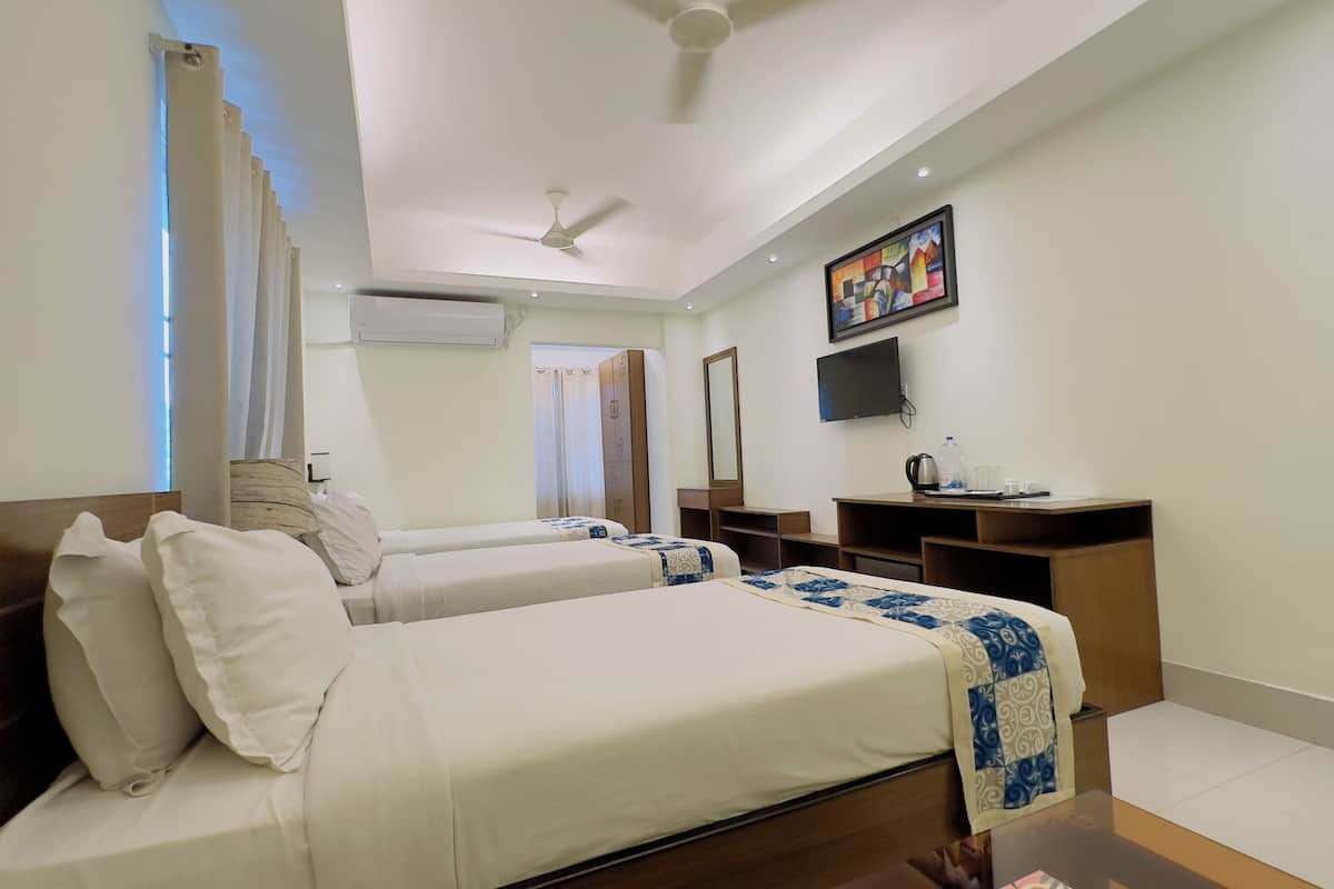 Une chambre d’hôtel avec deux lits, un bureau, une télévision et un ventilateur de plafond.