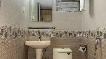 Ein kleines Badezimmer mit einem Standwaschbecken, Toilette und Dusche. Über dem Waschbecken befindet sich ein Spiegel und an der Wand ein Handtuchhalter.