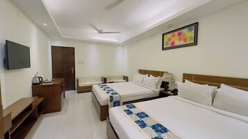 A hotel room with two single beds, a sofa, a desk with a kettle, and a television.