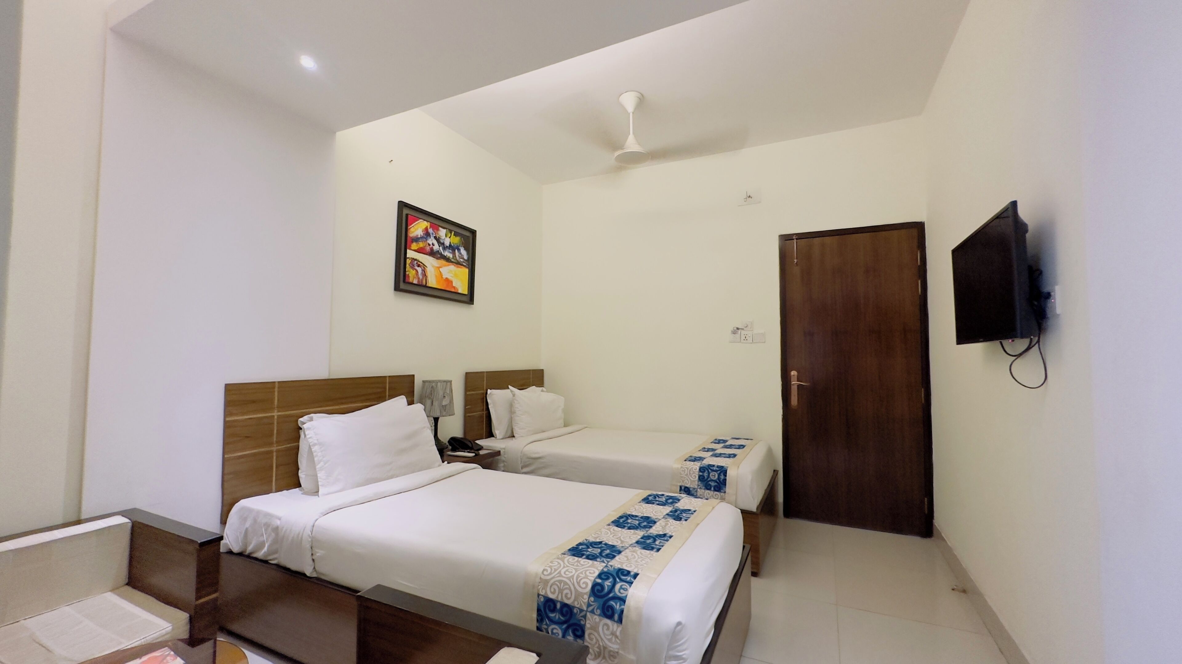 A hotel room with two beds, a wooden headboard, a ceiling fan, a TV mounted on the wall, and a door.