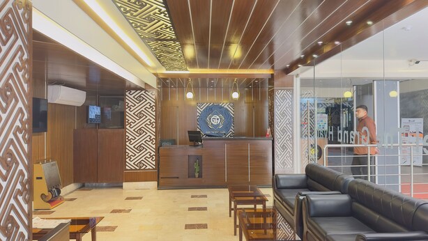 A hotel reception area with a wooden reception desk, a seating area with sofas, and a patterned wall design. - Hotel The Grand Hyatt Dhaka (Dhaka)