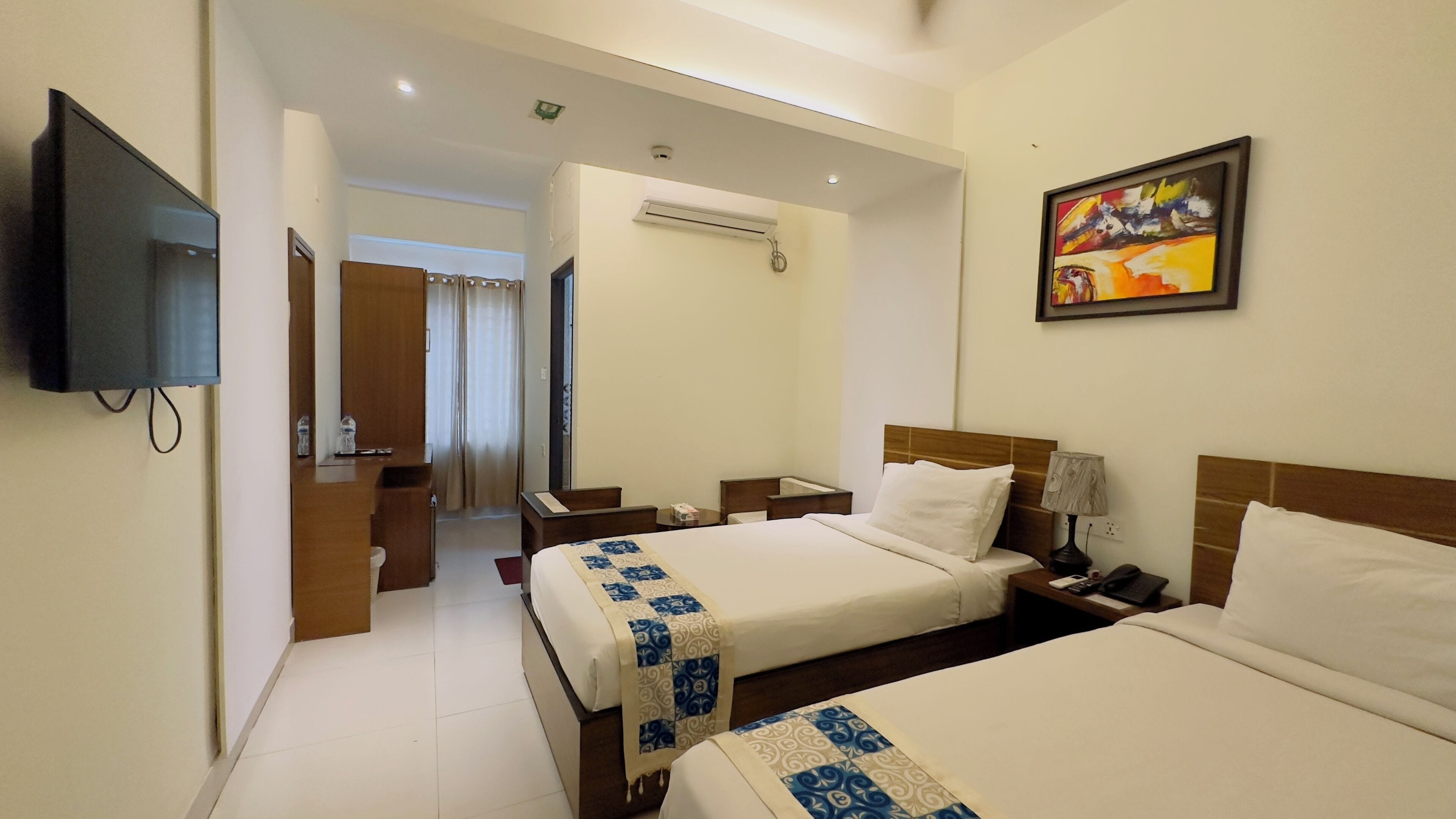 A hotel room with two beds, a TV, a painting, and an air conditioning unit.