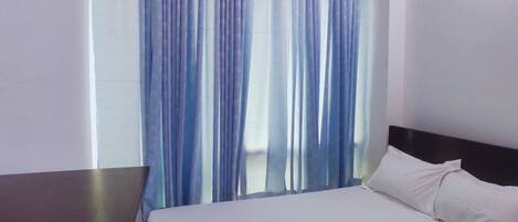 A hotel room with a bed, white bedding, and a window with blue curtains.